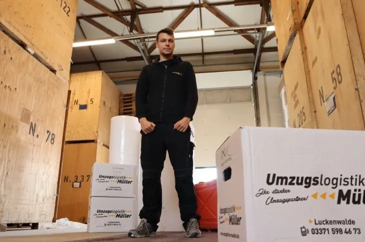umzugshelfer steht zwischen umzugskartons im lager
